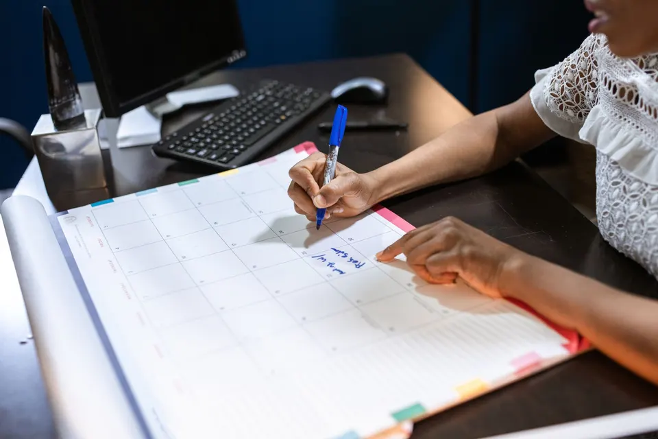 Hands writing a date on a monthly desk calendar with a blue pen