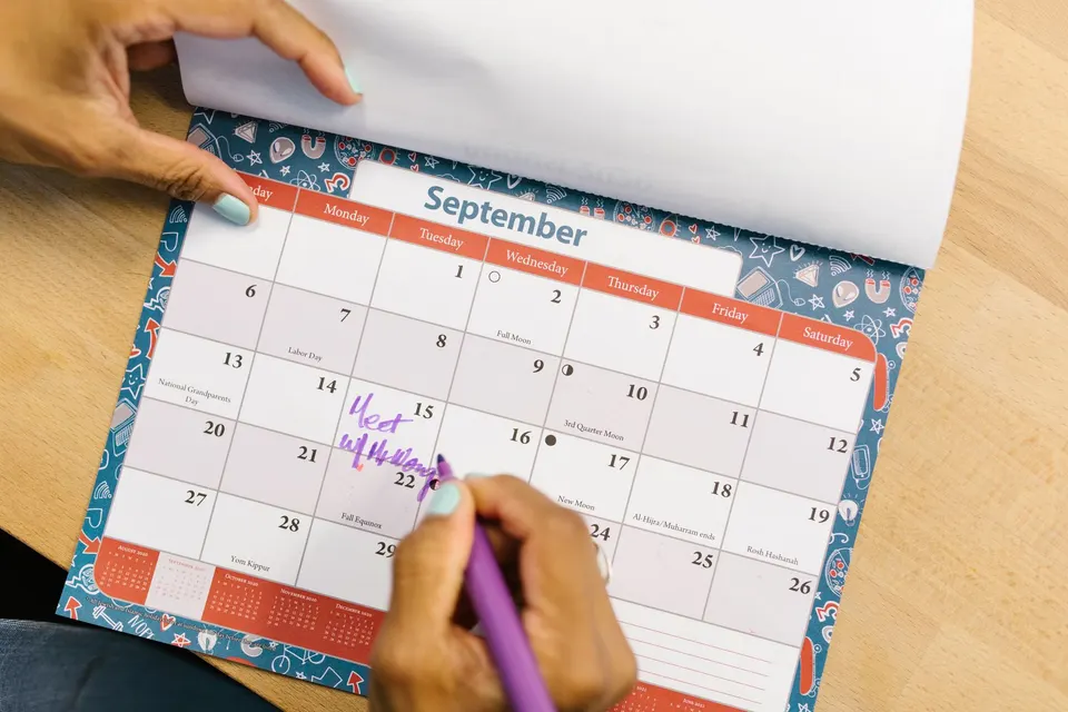 A wall calendar page being marked with a purple pen