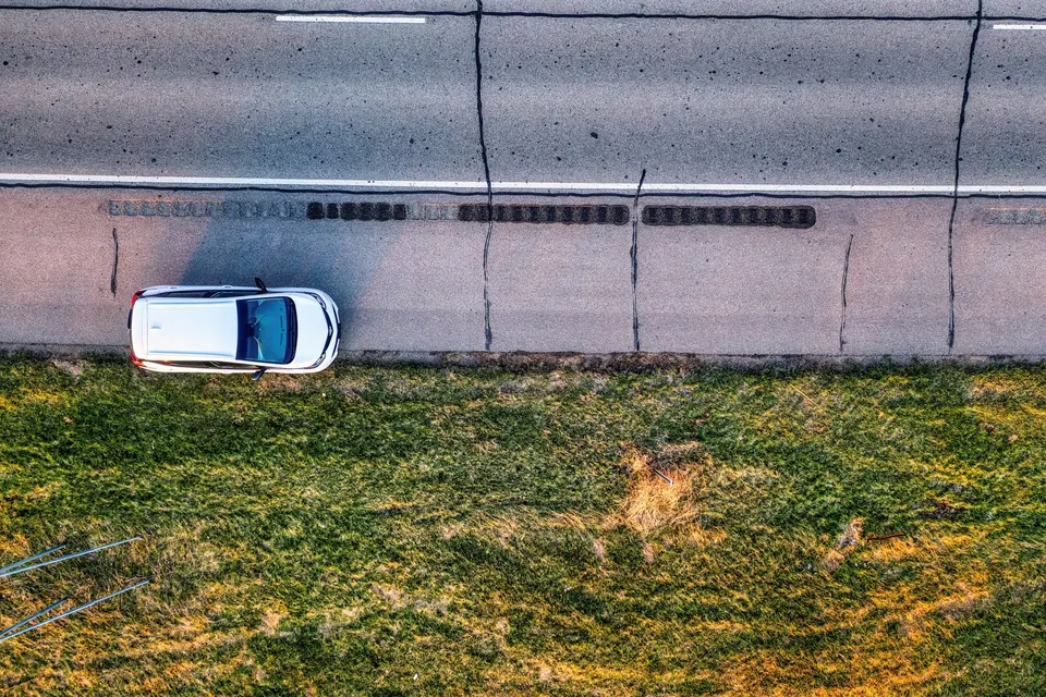 An aerial view of a white car stopped on the shoulder beside a road