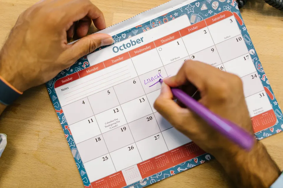 A hand writing a reminder on an October wall calendar