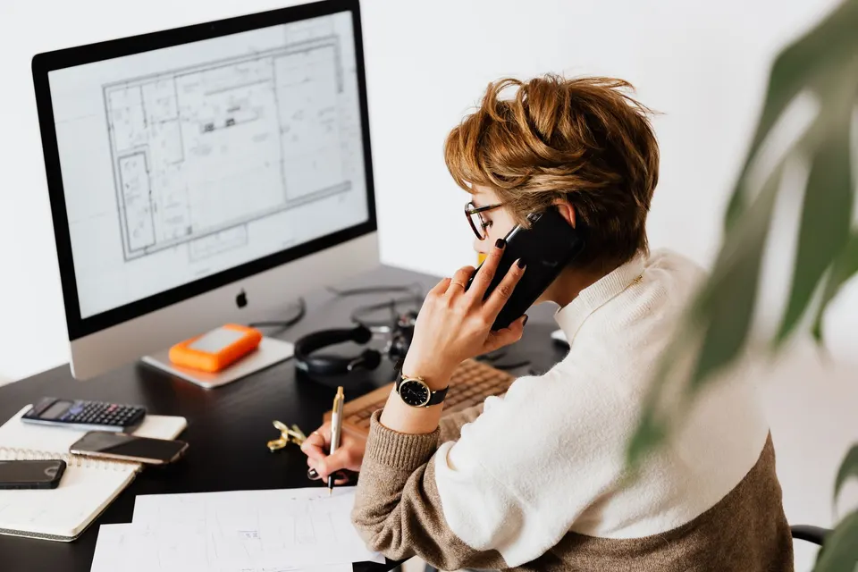 A person on a phone call taking notes on paper at a desk