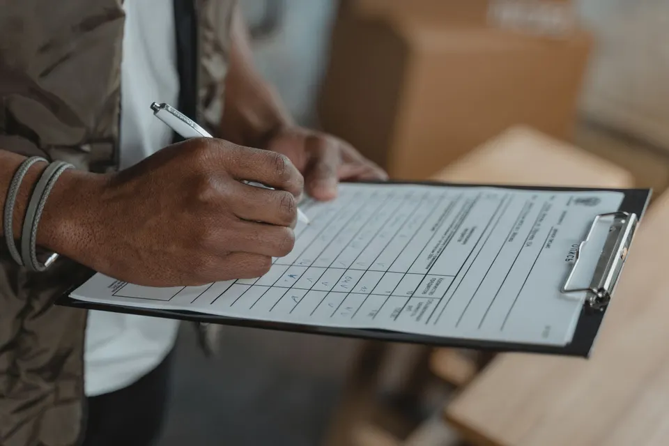 A hand holding a pen over a form on a clipboard