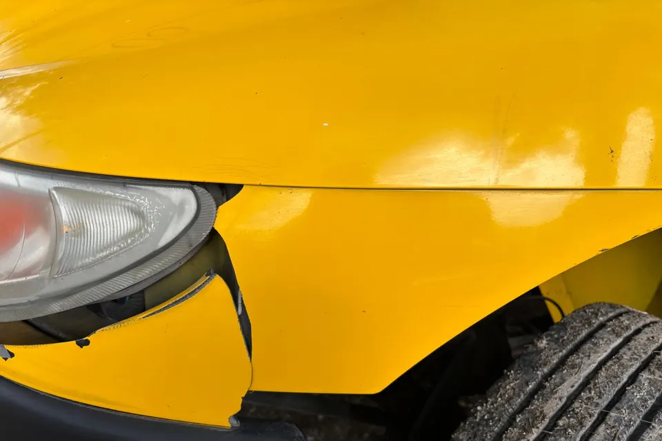A dented yellow bumper and cracked headlight on a car