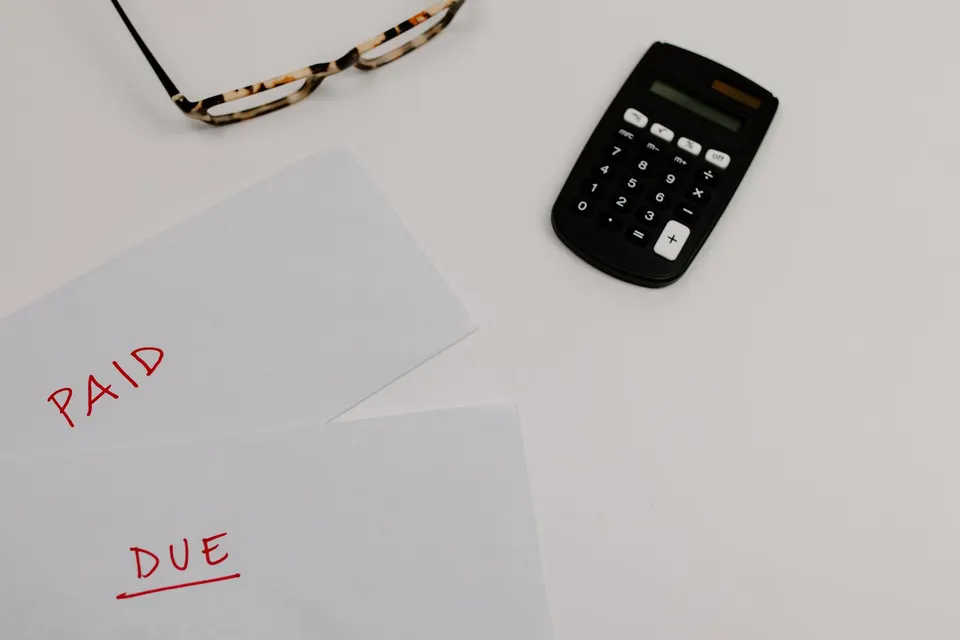 Bills marked paid and due on a desk next to a calculator and glasses